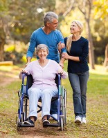 MIddle-aged couple walking arm in arm through a park while pushing their mother in a wheelchair