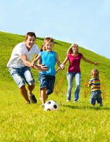 Healthy and happy family running through field chasing a soccer ball