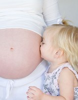 Cute blond toddler kisses her mothers pregnant belly